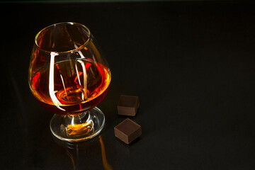 Cognac glass and chocolate on black background