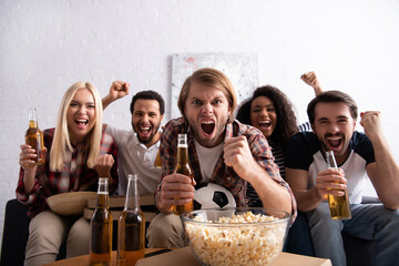 excited man shouting and showing win gesture while watching football game with multiethnic friends