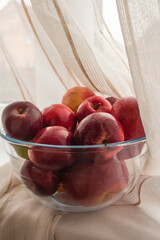 Lots of ripe apples in a transparent cup against the background of beige fabric