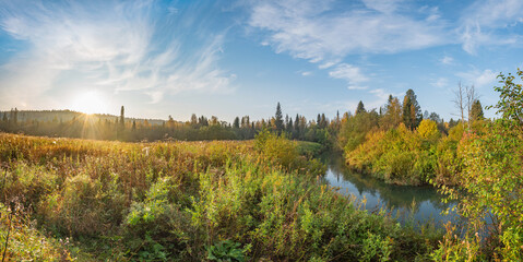 Panorama of the morning sunrise in the river valley, autumn colors on the trees and wet grass from the dew, beautiful blue sky in the clouds.