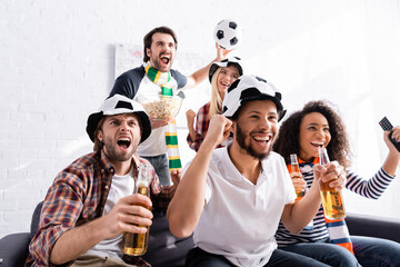 cheerful football fans holding beer and showing win gesture while watching championship