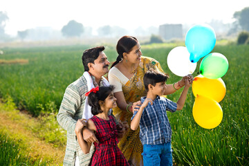 Happy indian family of farmer with balloons in agricultural field