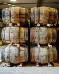 A stack of 6 traditional full whisky barrels, set down to mature, in a large warehouse