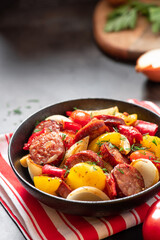 Sausages fried with peppers, tomatoes, and onions in a black plate on a dark background close-up. Free space for text. Sausages stewed with vegetables. Traditional Hungarian food lecho.