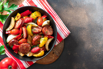Sausages fried with peppers, tomatoes, and onions in a black plate on a dark background top view. Copy space for text. Sausages stewed with vegetables. Traditional Hungarian food lecho.