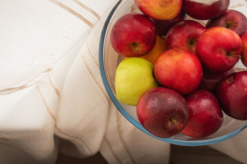 Lots of ripe apples in a transparent cup against the background of beige fabric