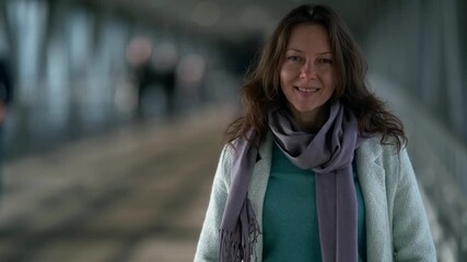 Portrait of a confident and cheerful middle-aged brown-haired woman who is standing in a crowded pedestrian crossing, wearing a coat and scarf.