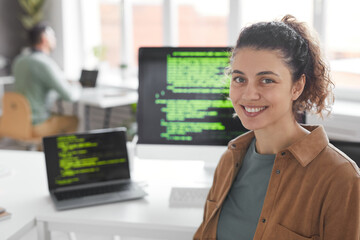 Portrait of professional programmer smiling at camera with computers on the table in the background
