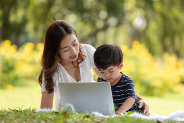 Asian family having fun mother and her son using laptop computer in the park together