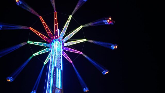 Swing tower ride, also known as vertical swing and flying tower covered with multicolored led lights spinning on the dark night black sky background 4K video