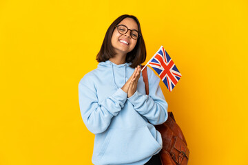 Young latin woman holding an United Kingdom flag isolated on yellow background keeps palm together. Person asks for something