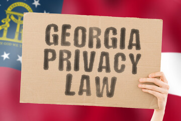 The phrase " Georgia privacy law " on a banner in men's hand with blurred Georgia's flag on the background. Private. Client. Market. Info. Information. Identify. Data