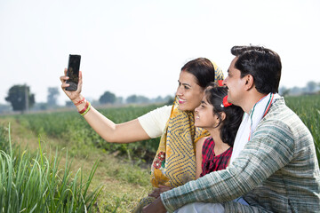 Happy indian family of farmer in agricultural field using phone