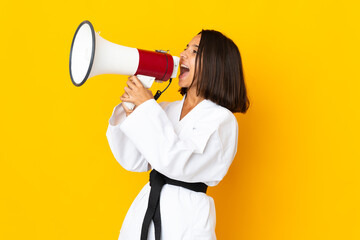 Young woman doing karate isolated on yellow background shouting through a megaphone
