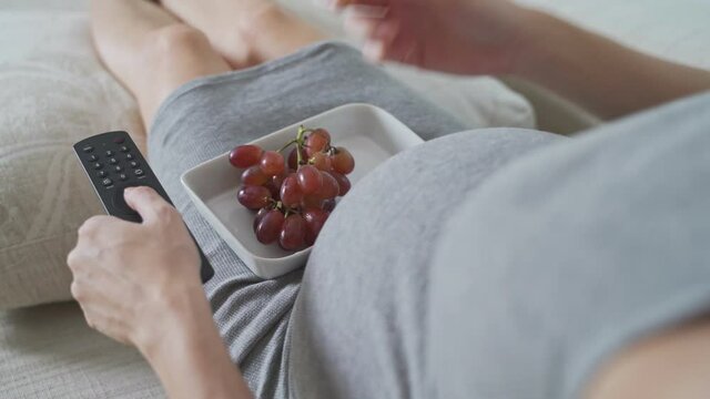 asian pregnant woman always hungry she watching television (TV) and eat grape fruit.