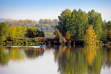 Fototapeta na wymiar Calmness river surface disturbs driving motor boat. Wonderful landscape of autumn forest on the background.