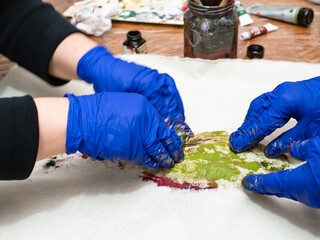 masterclass for Fish Drawing in Technique Monotype - hands in blue gloves press calico fabric to green colored fish on wooden table covered with plastic wrap