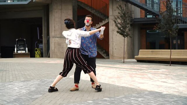 Man and woman clowns in costumes are meeting talking then dancing together outdoor.