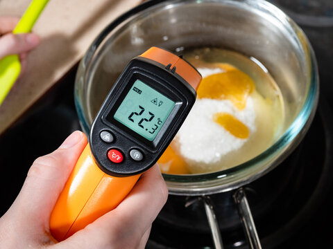 cooking sweet sponge cake at home - measuring temperature of ingredients in glass bowl on water bath by infrared thermometer on stove at home kitchen