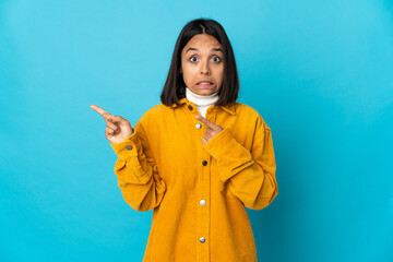 Young latin woman isolated on blue background frightened and pointing to the side