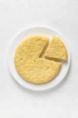 Potato omelette in portioned, a round white plate on a white background. Senital view. Vertical picture