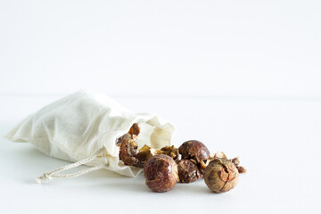Soap nuts falling out of linen bag on white background; isolated; alternative laundry detergent; organic; natural; ecologically alternatives