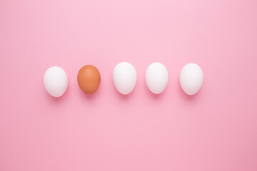 The concept of personality. Brown egg among white eggs on a pink background.