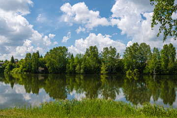 Reflection of green trees and blue sky with clouds in mirror surface of lake