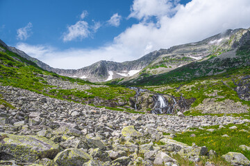 Rock ridge with snow and stone placers under blue sky. Summer trip to mountain valley. Atmospheric...