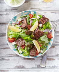 Tasty Salad with Grilled Beef Pieces, Cherry Tomatoes, feta Cheese and Kalamata Olives. Bright wooden background. Top view.	