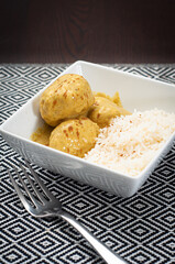 Danish meatballs in curry sauce served in a square white bowl with steamed basmati and garnished with cinnamon bark. A Nordic dish popular in all Scandinavian countries and inspired by Indian cuisine