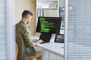 Mature technician sitting at his workplace in front of computer monitor and typing on laptop at IT...