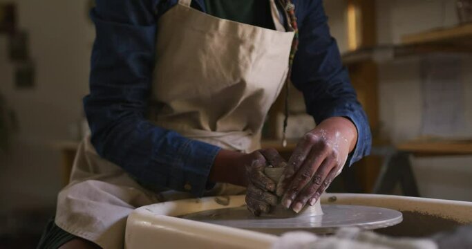 Mid section of female potter creating pottery on potters wheel at pottery studio