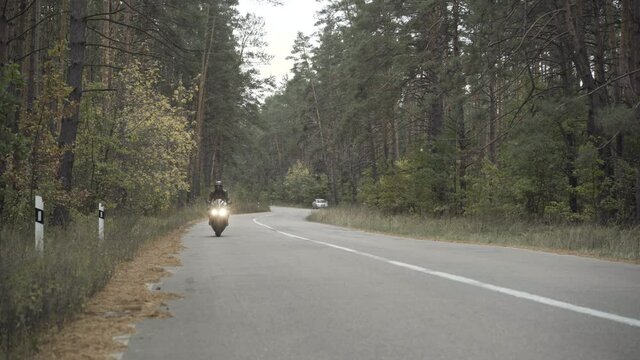 Extreme wide shot of man riding motorcycle to camera. Confident young man in leather jacket and helmet driving motorbike along the road outdoors. Lifestyle and racing concept.