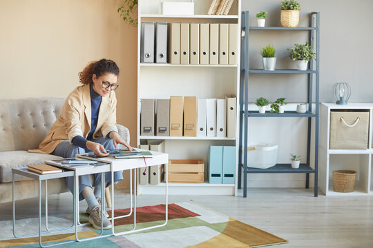 Female designer in eyeglasses sitting at the table and working with pictures at office