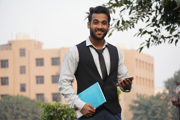 Fototapeta premium Image of happy Business wearing formal clothes smiling at camera with mobile in hands isolated over collage campus background