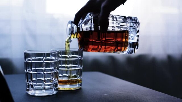 Pouring whiskey from bottle into glass on table. Space for text