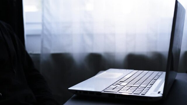 A man who opens his laptop and initiates a video conference. Working from home. Dark image. 
A possible hacker