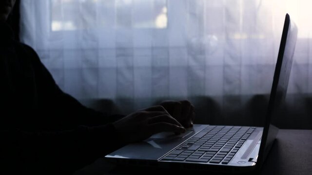 A man who opens his laptop and initiates a video conference. Working from home. Dark image. 
A possible hacker