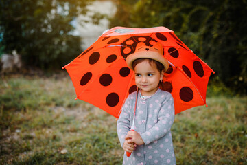 Portrait of a happy smiling little child 2 years old girl holding her red umbrella with polka dots outdoors.