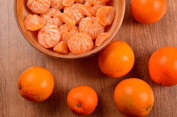 Freshly peeled tangerines in a clay bowl on a wooden background. Surrounded by whole fresh oranges
