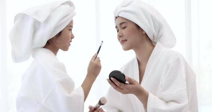 Mother and daughter in white bathrobes are having fun spa treatments.