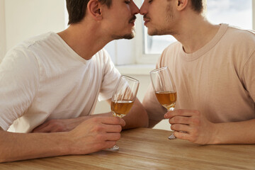 Gay couple of men drink wine from glasses and kiss at home