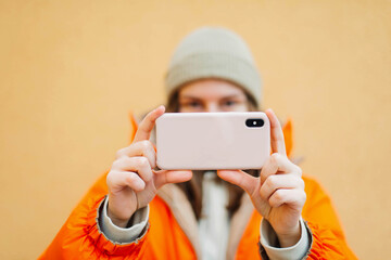 Young woman using smart phone while standing against yellow wall