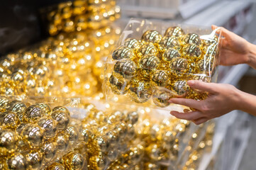 Woman holding packaging of golden balls of decorations on christmas tree in store