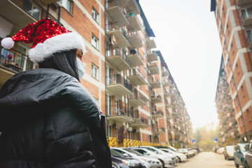 Obraz premium Female person in holiday season looks to the right with street view and houses in the background. Xmas at home on quarantine and curfew on Christmas.