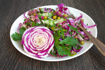 Fresh vegetable salad on a white plate on a dark wooden background. The concept of healthy food, diet, raw food, vegetarianism for menus, posts. Recipes with Chinese, Peking cabbage, cucumber and peas