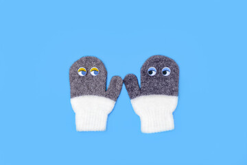 Pair of woolen knitted soft mittens with eyes. Concept of friendship, love, understanding. They kind of look at each other, hold hands. Half white, over gray. Men mitten is darker. Flat lay, top view