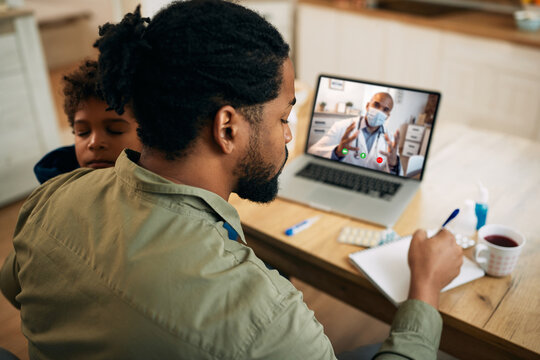 African American father taking notes while having video call with family doctor at home.