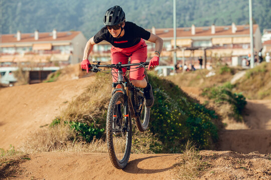 Sportswoman in black helmet and red sportswear with glasses riding mountain bike jumping in training track